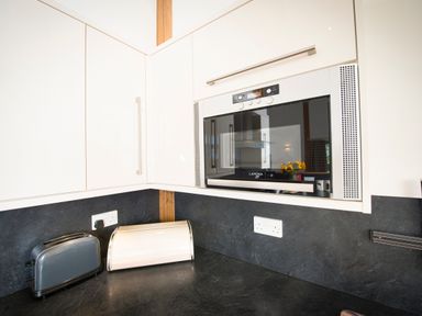 A kitchen corner with white cabinets a built-in Lamona microwave a grey toaster a white bread box and black countertops at Aurae in Cawdor near Inverness