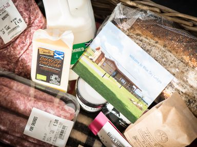 A basket with pork sausages minced meat cheddar cheese milk bread and a welcome card for Blue Sky Lodges