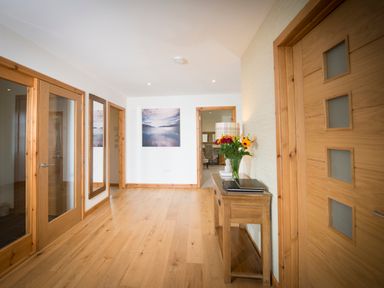 A hallway with wooden floors multiple wooden doors a console table with books a lamp and flowers and a wall mirror at Aurae in Cawdor near Inverness