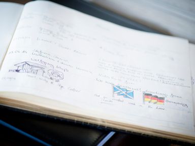 An open guestbook with handwritten notes drawings and small flags on a table at Aurae in Cawdor near Inverness