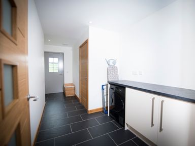 A utility room with a washing machine an ironing board a laundry basket and cupboards at Aurae in Cawdor near Inverness