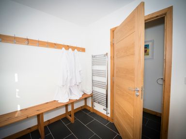 A changing room with wooden bench and hooks with white bathrobes hanging at Aurae in Cawdor near Inverness
