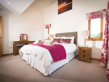 A bedroom with a bed with white bedding and pink throws two wooden bedside tables with lamps and a wooden dressing table with a mirror at Aurae Cawdor near Inverness