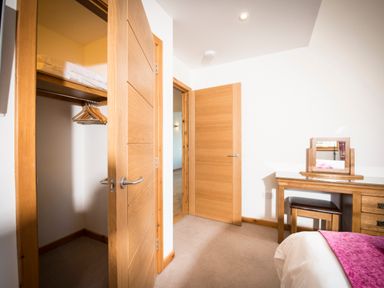 A bedroom with an open closet door and a wooden dresser with a mirror at Aurae in Cawdor near Inverness