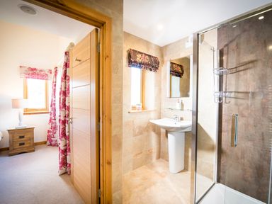 A bathroom with a sink and shower next to a bedroom with a nightstand and window at Aurae Cawdor near Inverness