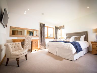 A bedroom with a bed a chair a desk and a wall-mounted TV at Aurae in Cawdor near Inverness
