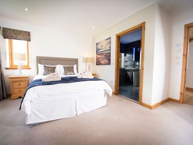A bedroom with a bed two bedside tables lamps and a view into a bathroom at Aurae in Cawdor near Inverness
