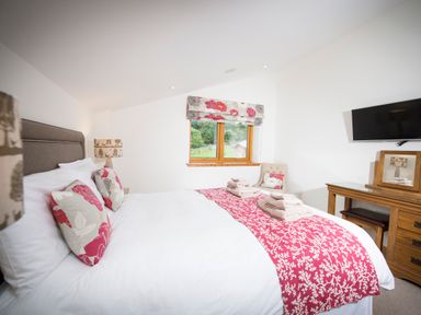 A bedroom with a double bed with folded towels bedside lamps and a wooden dressing table with a mirror at Aurae in Cawdor near Inverness