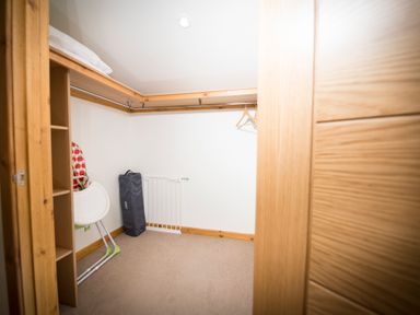A walk in closet with hanging rails shelves an ironing board and a baby gate at Aurae in Cawdor near Inverness
