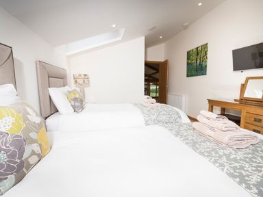 A bedroom with two single beds a wooden dressing table and a wall mounted TV at Aurae in Cawdor near Inverness