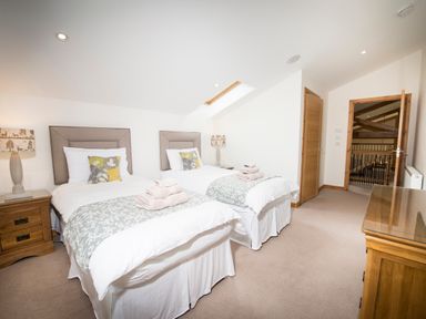 A bedroom with two single beds, bedside tables with lamps, folded towels on the beds and a wooden chest of drawers at Aurae in Cawdor near Inverness