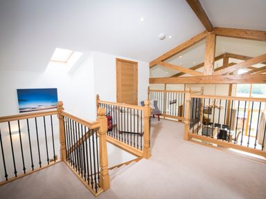 An upper landing area with wooden beams a chair and railings overlooking a dining area at Aurae in Cawdor near Inverness
