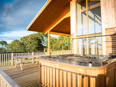 An outdoor deck with a hot tub and wooden picnic table at Aurae in Cawdor near Inverness