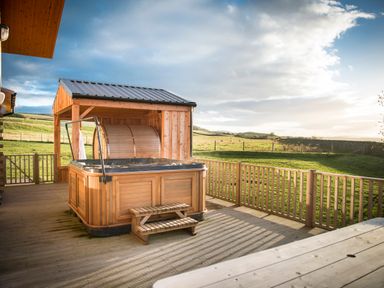 An outdoor wooden hot tub on a deck with a wooden fence and grassy field at Aurae in Cawdor near Inverness