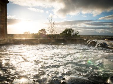 An outdoor hot tub with bubbling water and a view of trees and sky at Aurae in Cawdor near Inverness