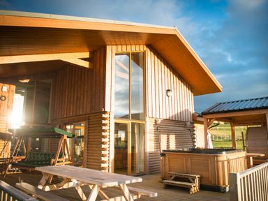 A wooden cabin with a swing, picnic table, and hot tub on the deck at Aurae in Cawdor near Inverness