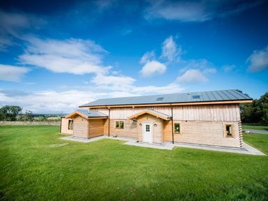 A wooden house with a metal roof on a lawn under a blue sky at Aurae in Cawdor near Inverness