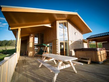 A wooden deck with a picnic table swing and hot tub outside a wooden house at Atlas in Cawdor near Inverness