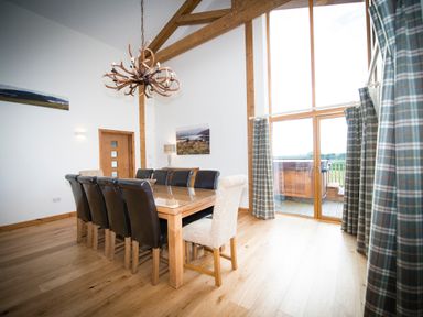 A dining room with wooden table and mixed chairs under an antler chandelier by a large window with plaid curtains at Atlas in Cawdor near Inverness