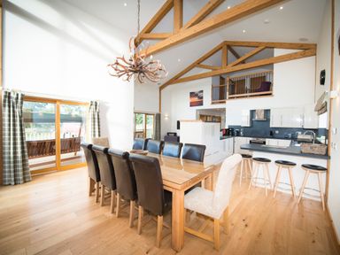 A kitchen and dining area with wooden beams a large wooden dining table with chairs and sliding glass doors at Atlas in Cawdor near Inverness