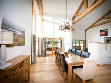 A dining room with a long wooden table with black and beige chairs a wooden sideboard and large windows at Atlas in Cawdor near Inverness