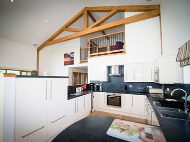 A kitchen with white cabinets black countertops and wooden beams at Atlas in Cawdor near Inverness