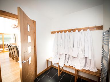 A small room with white robes hanging on hooks above a wooden bench and a wooden door leading to a dining area at Atlas in Cawdor near Inverness
