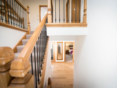 A staircase with wooden railing and black balusters leading to a hall with wooden floor and doors at Atlas in Cawdor near Inverness