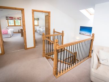 A hallway with wooden stair railing leading down and two bedrooms visible in the background at Atlas in Cawdor near Inverness
