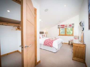 A bedroom with a double bed bedside lamp wooden dresser chair and open closet with hangers at Atlas in Cawdor near Inverness