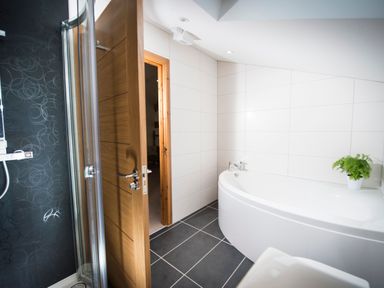 A bathroom with a wooden door a corner bathtub a shower with glass door and a potted plant on the bathtub ledge at Atlas in Cawdor near Inverness