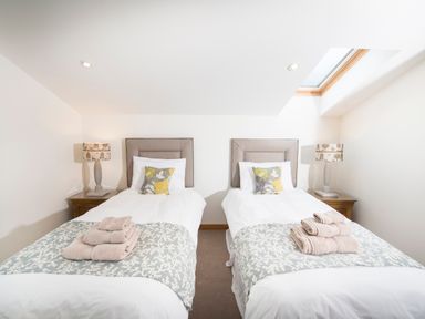 A bedroom with two single beds each with a patterned cushion and folded towels on a blanket at Atlas in Cawdor near Inverness