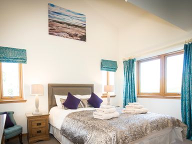 A bedroom with a double bed with folded towels two bedside tables with lamps blue curtains and a wall picture at Atlas in Cawdor near Inverness