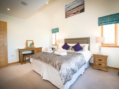 A bedroom with a double bed with folded towels on the bed two bedside tables with lamps and a dressing table with a mirror and stool at Atlas in Cawdor near Inverness