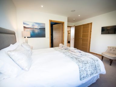 A bedroom with a bed with folded towels on it a chair a lamp a wall painting and wooden doors at Atlas in Cawdor near Inverness