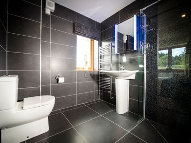 A bathroom with a toilet sink and shower with black tiles and a window at Atlas in Cawdor near Inverness