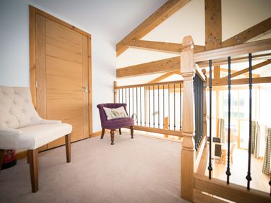 An upstairs landing with two chairs one beige and one purple and wooden railings at Atlas in Cawdor near Inverness