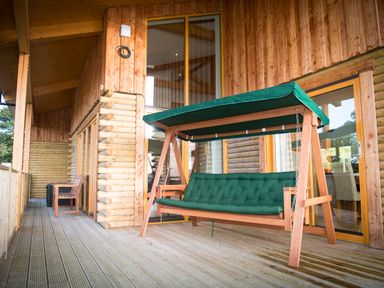 A wooden porch with a green cushioned swing and wooden bench at Atlas Cawdor near Inverness