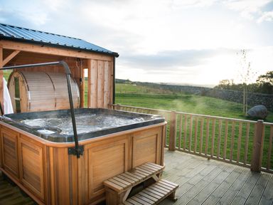 An outdoor hot tub with steam rising surrounded by wooden decking and railing at Atlas in Cawdor near Inverness