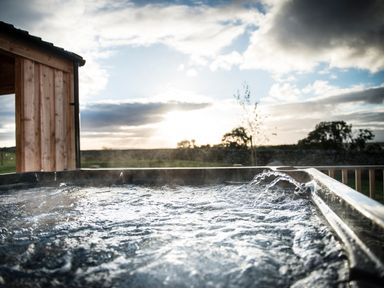 A bubbling hot tub outdoors near a wooden structure with trees and a cloudy sky at Atlas in Cawdor near Inverness