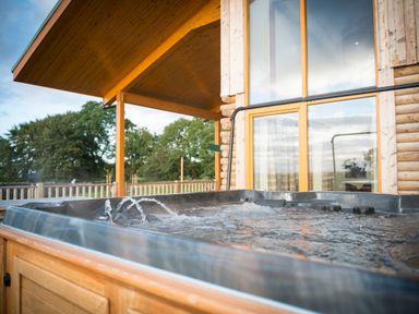An outdoor hot tub with water jets in front of a wooden house with large windows at Atlas in Cawdor near Inverness