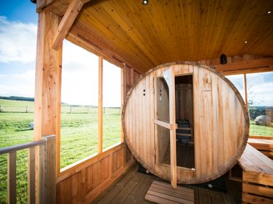An indoor wooden sauna with a round door and benches inside a wooden structure overlooking a grassy field at Atlas in Cawdor near Inverness