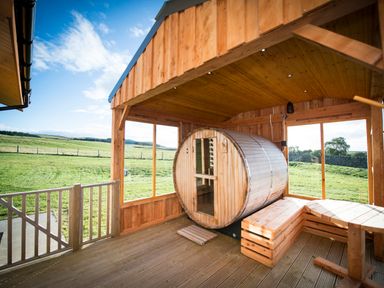 An outdoor wooden sauna and bench with a table on a veranda overlooking a grassy field at Atlas in Cawdor near Inverness