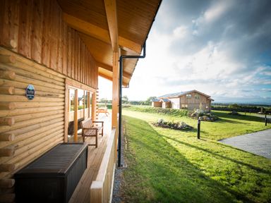 A wooden porch with a bench and storage box overlooking a grassy yard and another wooden building at Atlas in Cawdor near Inverness