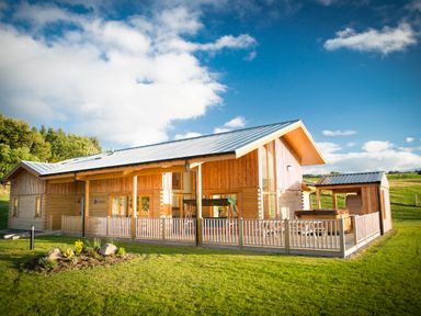 A wooden lodge with a metal roof on a grassy area with a fenced porch at Atlas in Cawdor near Inverness