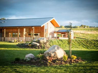 A wooden house with a metal roof surrounded by a garden with large rocks and grass at Atlas in Cawdor near Inverness
