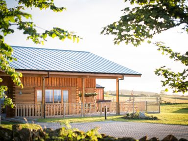 A wooden house with a metal roof and a fenced porch in a grassy area at Atlas in Cawdor near Inverness
