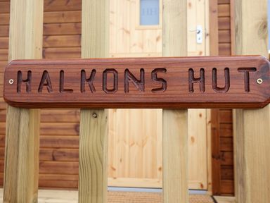 A wooden sign reading Halkons Hut attached to vertical wooden beams with a wooden door in the background at Shepherds Hut in Garthorpe near Scunthorpe