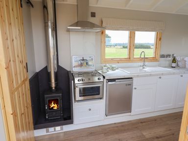A kitchen with a wood stove cooker sink dishwasher and window at Shepherds Hut in Garthorpe near Scunthorpe