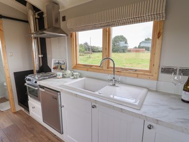 A kitchen with a sink under a window and a stove next to a refrigerator at Shepherds Hut in Garthorpe near Scunthorpe